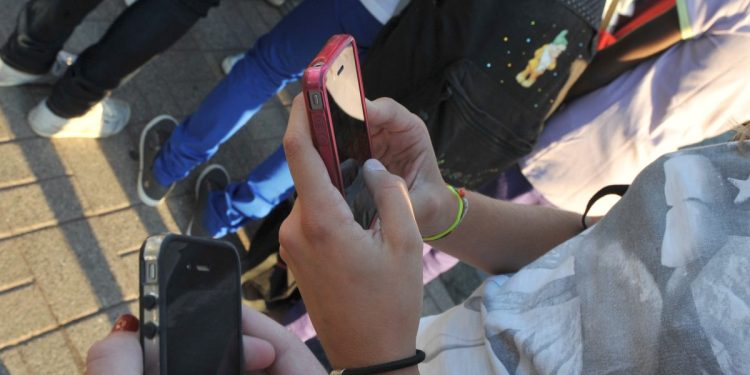 Studentesse all'ingresso della scuola con il telefonino (Ansa)