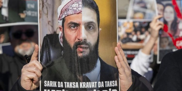 Cartello di protesta che ritrae il presidente siriano al Sharaa, (ex) jihadista dello Stato islamico (Ansa)